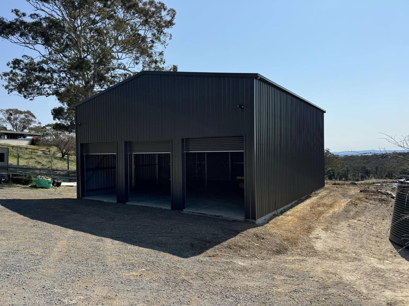 Black multi-bay steel garage with roller doors and a gravel apron