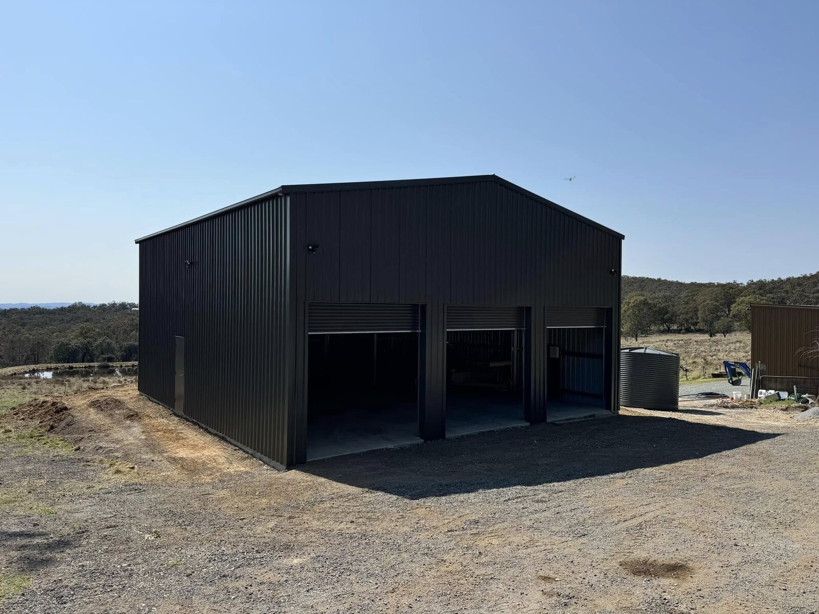 Custom black steel garage with roller doors built on a country property