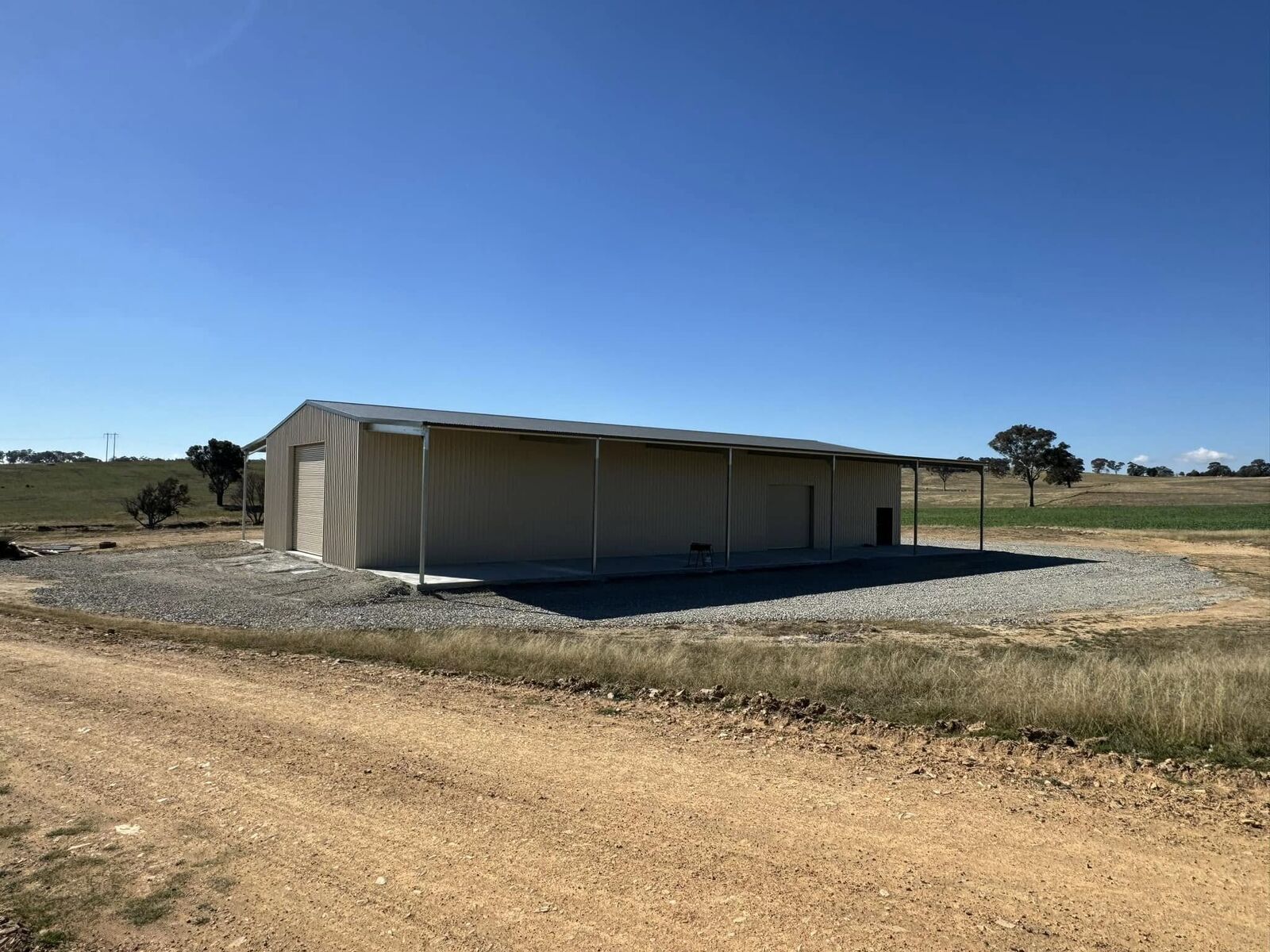 Wide low-profile cream Colorbond farm shed in a rural paddock