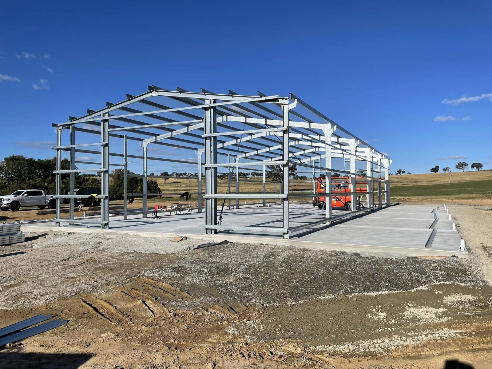 Large steel portal frame being erected for a wide-span shed under a clear sky
