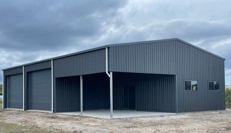 Wide grey Colorbond steel shed with roller doors on a cleared rural block