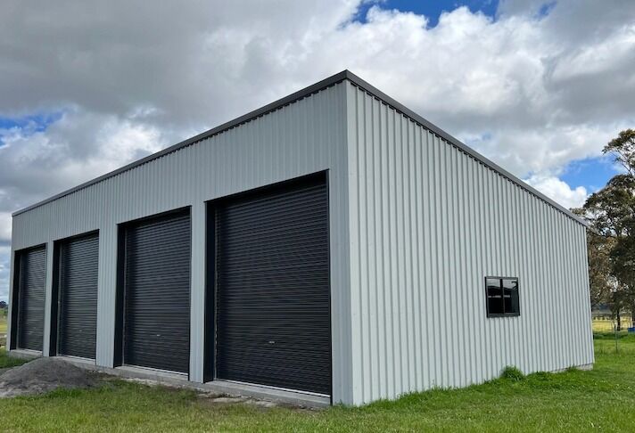 Cream skillion-roof garage with multiple black roller doors on a grassed block