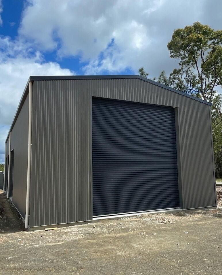 Grey Colorbond shed with a dark roller door and gravel surround